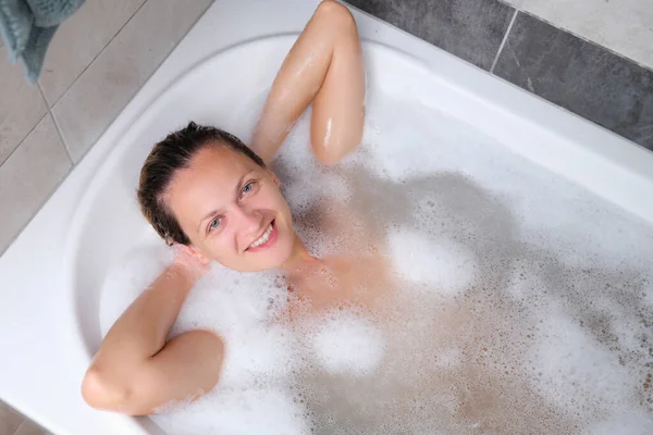 Vacker ung leende kvinna ligger i badkaret ovanifrån — Stockfoto
