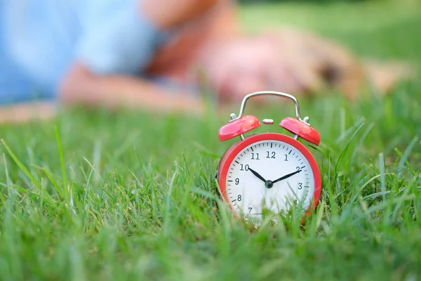 Red alarm clock on grass in background lies woman — Stock Photo, Image
