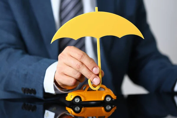 Man worker in suit hold wooden umbrella over yellow car model, symbol for car protection — Foto de Stock