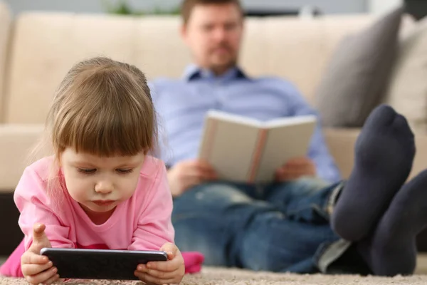 Niña jugar con el dispositivo de teléfono inteligente, entretenimiento digital para niños, papá libro de lectura — Foto de Stock