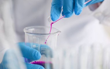 Bilim adamı tıbbi kimya laboratuvarında mataradan pembe sıvı döküyor.