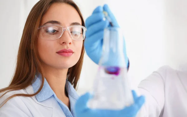 Scientist coworkers in glove add pink liquid to flask, microbiology science — стоковое фото