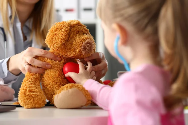 Little girl touch heart of stuffed teddy bear, listen with stethoscope, check heartbeat — 图库照片