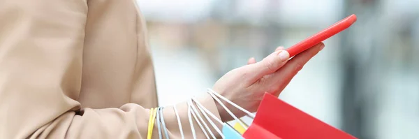 Vrouw met smartphone en pakketten in haar hand — Stockfoto