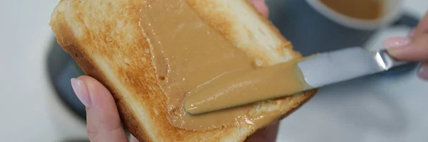 Mujer dabs mantequilla de maní en tostadas con un cuchillo —  Fotos de Stock