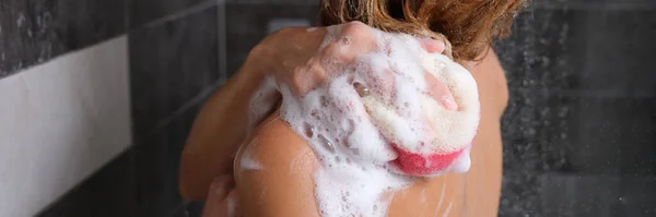 Mulher no chuveiro com uma esponja ensaboada lava seu corpo — Fotografia de Stock