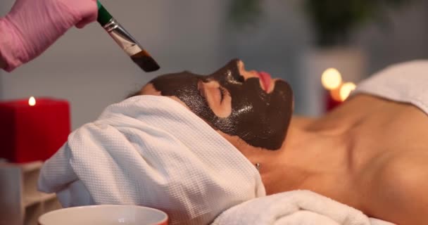 Young woman applies detoxifying clay mask to face in beauty salon — Stock Video