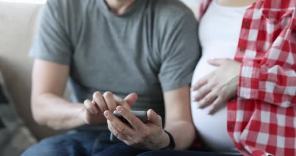 Zwangere vrouw en echtgenoot kiezen online winkel voor goederen voor pasgeborenen — Stockvideo