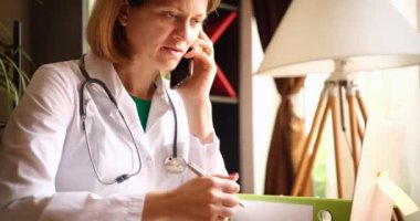 Gülümseyen güzel bayan doktor klinikteki iş yerinde telefonla konuşuyor.