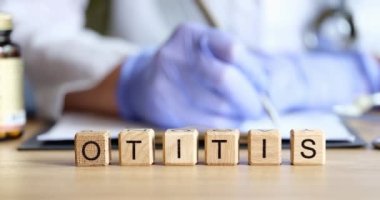 Doktor, ahşap küplerin arka planına otitis 4k kelimeleriyle tıbbi belgeler yazıyor.