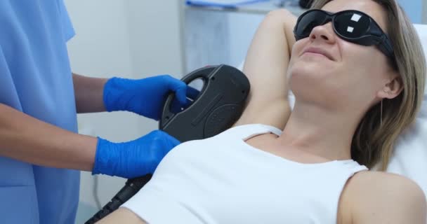 Woman client in protective glasses having laser hair removal of armpit in beauty salon 4k movie — Stockvideo