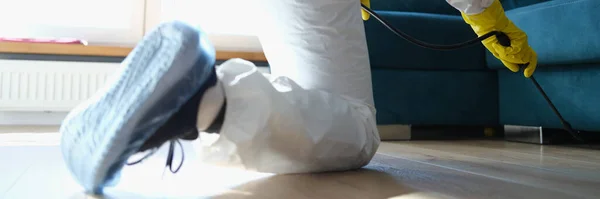 Человек в защитном костюме распыляется под диваном — стоковое фото