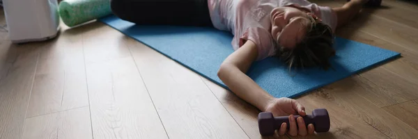 A woman with dumbbells lies on the floor at home — Stock Photo, Image