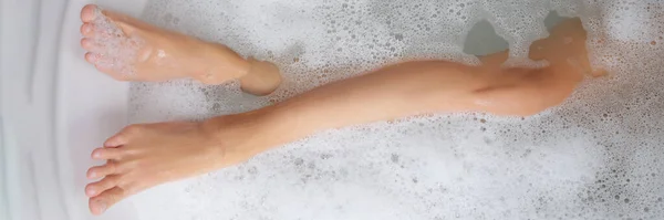 Delgadas piernas femeninas en una bañera con agua jabonosa — Foto de Stock