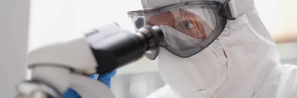 Un hombre con traje protector y máscara mira a través de un microscopio — Foto de Stock