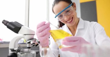 Gülümseyen bilim adamı laboratuardaki test tüpünde sarı yağı inceliyor. Kimya kliniğinde yağ ve kayganlaştırıcılar