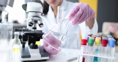 Laboratuvar bardakları ve deney tüplerinde şeffaf sıvı bulunan matarayı tutan bilim adamının eli. Kimyasal ve araştırma laboratuvarı ve geliştirme kavramı