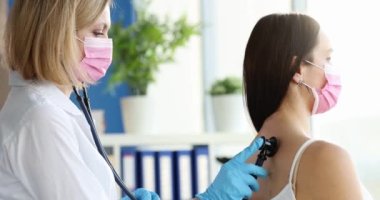 Tıbbi maskeli profesyonel bir doktor kadın hastanın akciğerlerini dinler. Akciğerlerin zatürree ve ilaç konseptinde incelenmesi.