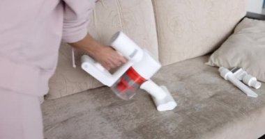 Oturma odasındaki kanepeyi temizlemek için beyaz kablosuz elektrik süpürgesi kullanıyor. Döşeme mobilya temizleme konsepti