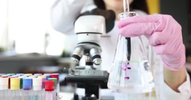 Bilim adamı şeffaf matarayı sıvı ile tutuyor ve mor toksin reaksiyonunu eşeliyor. Laboratuvar konseptinde kimyasal araştırma