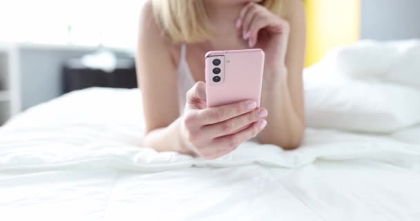 ベッドの上に寝そべってオンラインビデオを見ているスマートフォンを持つトリミングされた女性 テクノロジーの自由な時間とコミュニケーションの概念 — ストック動画
