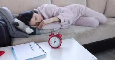 Genç kadın kanepede uyuyor ve çalar saati kapatıyor. Uyku yorgunluğu ve depresyon kavramı