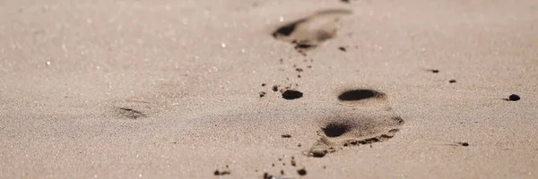 Close-up of human foot prints on golden beach sand. Footsteps in sandy beach. Time to travel and relax. Summer vacations, holidays and travelling concept