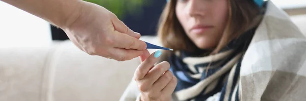 Portrait of someone give young woman thermometer to measure temperature. Sick woman stay at home and get treatment, feeling unwell. Sickness, virus concept