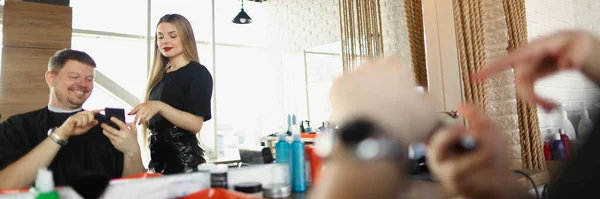 髪の毛のマスターイメージを示す男性のクライアントの肖像画彼は電話で望んでいる 有資格の理容師の女性は指示に従う 美容室 ファッションコンセプト — ストック写真