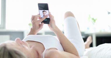 Yatakta yatan bir kadın akıllı telefondan online başvuruda bir erkeği seçer. İnternet randevusu, evlilik ajansı.