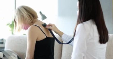 Doktor öksüren bir kadının akciğerlerini dinliyor, yakın plan. Koronavirüs ve zatürree belirtileri.