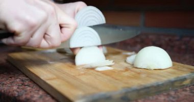 Bir adam ahşap bir tahtanın üzerinde soğan kesiyor, elleri yakın plan. Mutfakta yemek pişirmek, vejetaryen olmak.