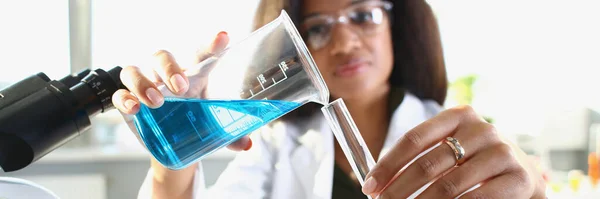 Dark-skinned woman scientist pouring blue liquid into a test tube, close-up, blurry. Experimenting with drugs