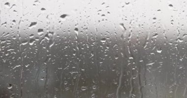 Yağmur damlaları cama vurur, yakın plan. Yoğunluk gri arka planda akar, mevsimsel yağış