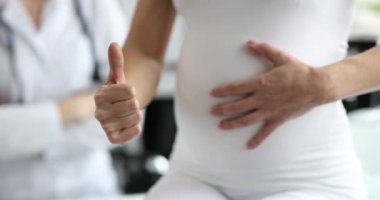 Hamile bir kadın karnını okşar ve baş parmağını kaldırır. Kadın danışmanlığı, doğum öncesi muayene.