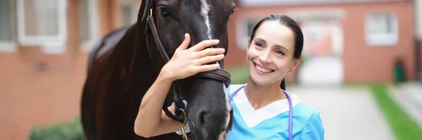 Beautiful woman, veterinarian stroking a horse, close up. Qualified friendly employee of the veterinary clinic