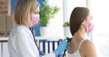 Terapist, koruyucu maskeli hastaların ciğerlerini dinler. Zatürree gribi ve covid-19 konsepti