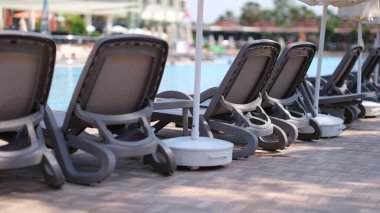 Yüzme havuzunun yanında bir sürü boş güneşlik ve güneşlik duruyor. Tatil konsepti