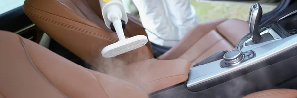 Close-up of hazmat worker cleansing car interior with spray disinfectant and steam heat. Disinfect auto upholstery from virus. Covid prevention concept