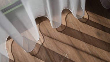 Öğlen güneşinde beyaz perdeler odadaki kahverengi ahşap zeminde gölge yaratır. Beyaz şeffaf dederon kavramı