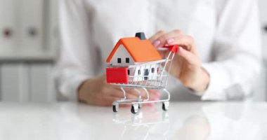 Alışveriş arabasındaki klasik ev modeli emlakçı tarafından taşınıyor. Kredi konseptiyle ev almak