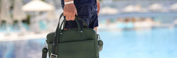 Man with bag for documents walking along edge of swimming pool closeup. Business work at resort concept