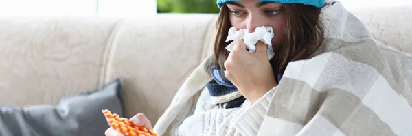 風邪をひいた女性は錠剤とハンカチでソファに座っています 季節病の概念 — ストック写真