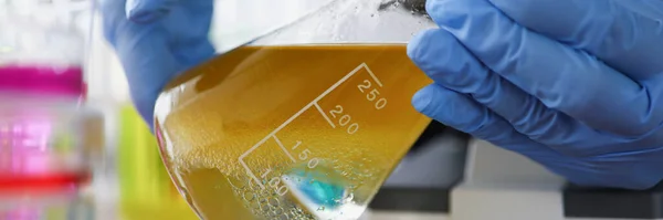 Zbliżenie Naukowca Rękawiczkach Ochronnych Trzymającego Kolbę Żółtym Płynem Laboratorium Chemicznym — Zdjęcie stockowe