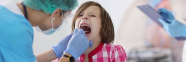 Küçük çocuğun portresi, kontrol için ağzı açık, boğazı ağrıyan, aletli çocuk doktoru randevusu. Genç bayan doktor muayenesi. Tıp konsepti