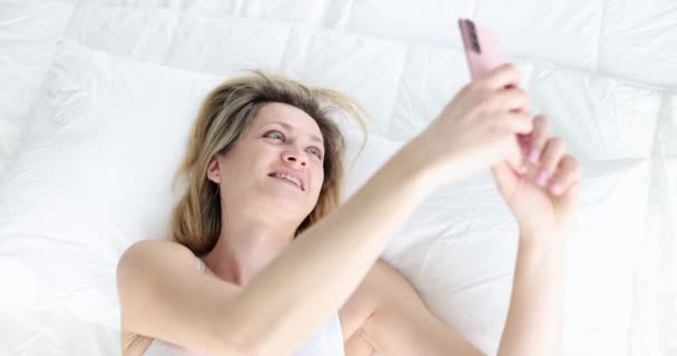 Attractive Young Woman Smiling Looking Smartphone Camera While Lying Bed — Stock video