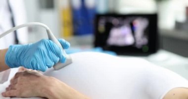 Doktor modern klinikte genç hamile bir kadının karnını ultrasonla muayene ediyor. Hamile kadın jinekologdan ultrason alıyor.