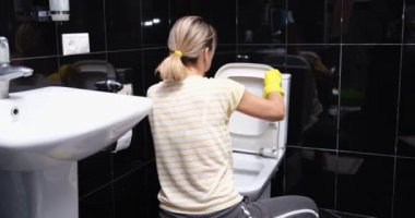 Eller evdeki tuvalet kağıdıyla klozet kapağını temizliyor. Sarı lastik eldivenli kadın tesisat konseptini temizler ve yıkar.