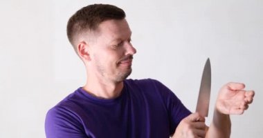 Smiling young male shows how to cut vein on arm. Knife games and jokes concept