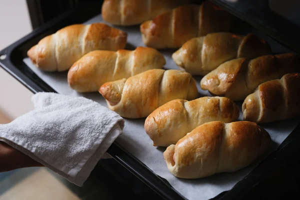 Woman takes a baking sheet with croissants from oven in kitchen. Delicious fresh cooked croissants